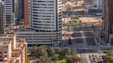 Barsha Heights bölgesindeki gökdelenler ve camii ve Yeşiller bölgesindeki alçak katlı binalar gölgeler hızla hareket ediyor. Kavşağın etrafında palmiyeler ve ağaçlarla Dubai silüeti