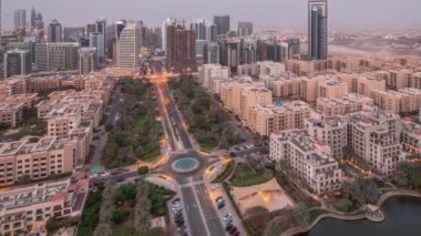 Barsha Heights bölgesindeki gökdelenler ve Greenens bölgesindeki alçak binalar hava gününden geceye geçiş zamanları. Palmiyeleri ve yürüyen göleti olan Dubai silüeti