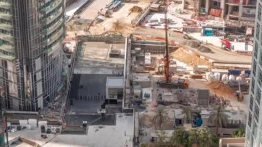 Crane ve buldozer yeni gökdelen hava zaman çizelgesinin şantiyesinde çalışıyorlar. Arazi temizliği, not verme, havuz kazma, siper kazma ve temel kazma. Sürüngen traktörü ve toprak hareket ediyor.