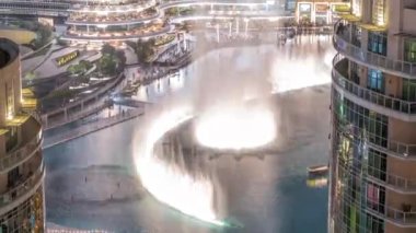 Dubai 'de gökdelenler arasında gece görüşü etrafında yürüyen çeşmeler var. Eski kentte geleneksel evleri olan bir mimari. Alışveriş merkezinin yakınındaki gösteriyi izleyenler