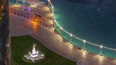 Çimenli yeşil çimenli park, çeşmelerin yanında gece vakti anıtı var. Dubai şehir merkezindeki yapay göl çevresindeki kuleler. Palmiyeler ve ağaçlarla yukarıdan görünüm