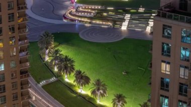 Fıskiyelerin yanındaki yeşil çimenli park. Dubai şehir merkezindeki yapay göl çevresindeki kuleler. Palmiyeler ve ağaçlarla yukarıdan görünüm