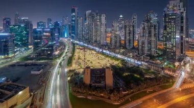 Business Bay havacılık panoramik gece zaman çizelgesinde aydınlatmalı modern kuleleri olan Bay Avenue, Dubai, BAE. Büyük otoparkın yakınındaki yolda trafiği olan gökdelenler.