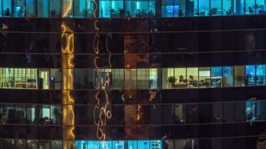 Gece karanlığında parıldayan camlı bir gökdelenin ofis pencereleri şehrin ışıklarını yansıtıyor. Akşamları aydınlık kule