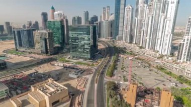 Business Bay havacılık panoramik zaman diliminde modern kuleleri olan Bay Avenue, Dubai, BAE. Büyük otoparkın yakınındaki yolda trafiği olan gökdelenler.