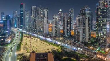 Bay Bulvarı 'nda aydınlatmalı modern kuleler Business Bay havacılık panoramiklerinde yerleşim alanları var. Tüm gece boyunca zaman çizelgesi, Dubai, BAE. Büyük otoparkın yakınında ışıkları kapanan gökdelenler.
