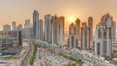 Günbatımında Bay Bulvarı 'nda Business Bay havacılık panoramik zaman dilimi, Dubai, BAE' de modern kuleler inşa edildi. Büyük otoparkın yakınındaki yolda trafiği olan gökdelenler.