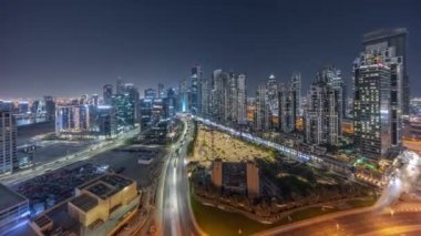 Bay Bulvarı 'nda aydınlık modern kuleler Business Bay hava sahasında gece vakti panorama, Dubai, BAE' de yerleşim alanı. Büyük otoparkın yakınındaki yolda trafiği olan gökdelenler.