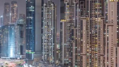 Business Bay hava sahasında modern kuleleri olan Bay Bulvarı. Gece uçuşu, Dubai, BAE. Pencerelerinde parlayan ve yanıp sönen halatlar olan gökdelenler.