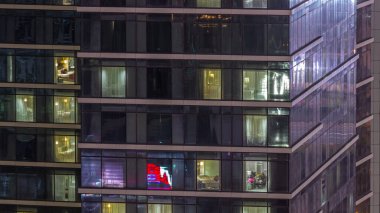 Gece karanlığa bürünmüş gökdelen perdeleri olan apartman pencereleri şehrin ışıklarını yansıtan zaman ayarlı yansıtmalı. Aydınlatılmış kuleler