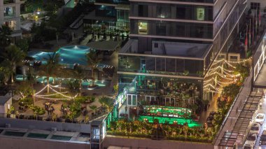 Açık havada yüzme havuzu olan rahat bir restoran ve barın hava manzarası. Dubai 'deki iş yerlerinde masalarda oturan insanlar..