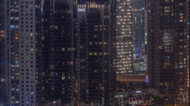 Dubai 'deki Business Bay' de parlayan pencereleri olan gökdelenler. Çimenli ve palmiyeli park, Birleşik Arap Emirlikleri