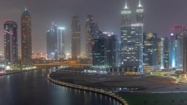 Dubai İş Körfezi 'ndeki gökdelenlerin şehir manzarası ve su kanalları gece zaman çizelgesi. Aydınlatılmış kuleleri ve rıhtımı olan modern gökyüzü. Uluslararası bir iş merkezi.