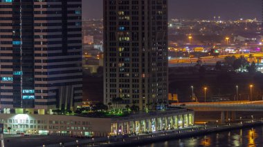 Dubai İş Körfezi 'ndeki gökdelenlerin şehir manzarası ve su kanalları gece zaman çizelgesi. Yanan kuleleri ve arkasında villaları olan modern gökyüzü. Uluslararası bir iş merkezi.