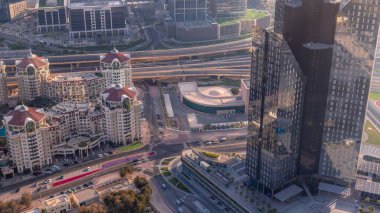 Dubai şehir merkezindeki üst geçit kavşağında yoğun trafik var. Gün batımında alışveriş merkeziyle cam kuleler arasında bir çok araba kavşakta hareket ediyor.