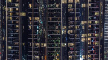 Yüksek sınıf bir binanın dairelerinde gece vakti aydınlatılmış panoramik pencereler. Gökdelende parlayan ışıklar ve balkonlar