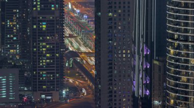 Dubai şehir merkezindeki parlayan camlı gökdelenler arasındaki karayolu ve üstgeçit. Metro istasyonunun yakınındaki kulelerde parlayan pencereler ve yukarıdan yoğun trafik.