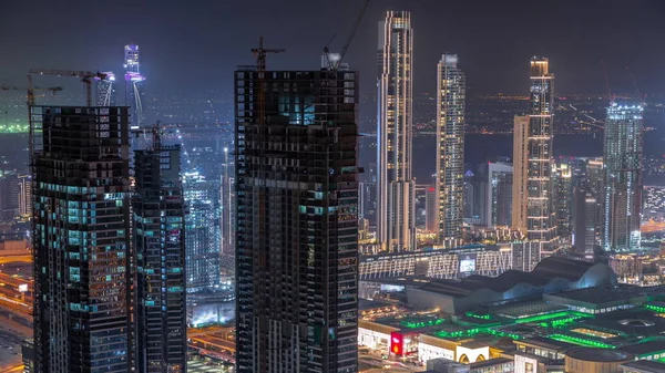 Dubai downtown with large-scale construction of a residential complex with a view of construction cranes aerial night timelapse. Illuminated skyscrapers and shopping mall