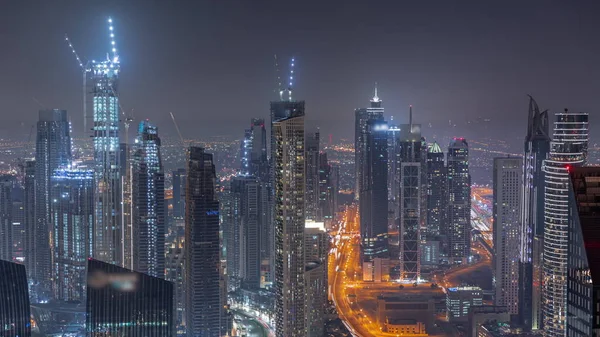 Downtown skyline with modern architecture form above night timelapse. Aerial panoramic view of Dubai business bay illuminated towers.