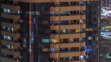 Aydınlatılmış çalışma odası saatleriyle apartman penceresi ön cephesinin gece görüşü. Gökdelende bir sürü balkonlu yanıp sönen ışık.