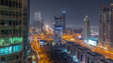 Dubai şehrinin gökyüzü panoramik manzaralı metro ve arabaları şehrin en işlek karayolu gece zaman çizgisinde ilerliyor. Parlak pencereli gökdelenlerle çevrili kavşak