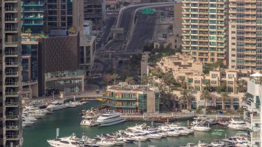Limanda yüzen yatların hava görüntüsü zaman ayarlı. Dubai Marina 'da limana yakın park edilmiş beyaz tekneler var. Bir yol kavşağında trafik