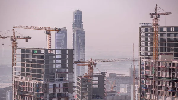 Dubai downtown with large-scale construction of a residential complex with a view of construction cranes aerial timelapse. Building activity with skyscrapers on a background
