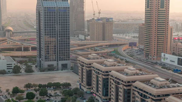 Aerial view of Dubai International Financial District with many skyscrapers timelapse. Traffic on a road near parking lot with trees. Junction on a background. Dubai, UAE.