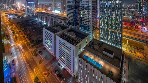 Aerial view of Dubai International Financial District with many illuminated skyscrapers night timelapse. Traffic on a road near multi storey parkings with rooftop swimming pool. Dubai, UAE.