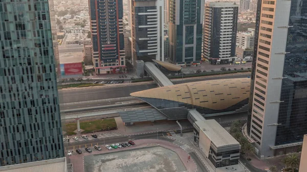 Busy Sheikh Zayed Road aerial timelapse, metro station with railway and modern skyscrapers around in luxury Dubai city. Heavy traffic on a highway with many cars. United Arab Emirates