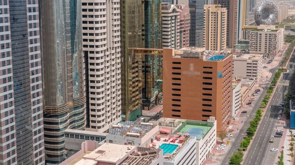 Aerial view of Dubai International Financial District with many skyscrapers timelapse. Traffic on a road near multi storey parking with rooftop swimming pool and solar panels. Dubai, UAE.