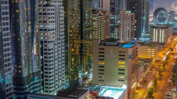 Aerial view of Dubai International Financial District with skyscrapers night timelapse. Traffic on a road near multi storey parking with rooftop swimming pool and tennis court. Dubai, UAE.