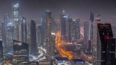 Şehir merkezinin ufuk çizgisi, modern mimari biçimle gece zamanının üstünde. Dubai iş hangarı kulelerinin hava görüntüsü. Gökdelenler arasındaki yollarda trafik