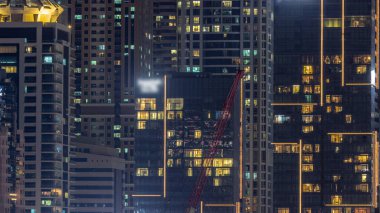 Parlak pencereli, dış apartman manzaralı bir zaman çizelgesi. Dubai marinasında ışıkları olan gökdelenli bir gökdelen. Crane inşaat alanında.