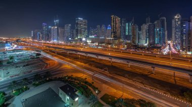 Dubai Marina gökdelenleri ve Şeyh Zayed yolu ile metro demiryolu gece panoramik zaman çizelgesi. Modern kulelerin yakınındaki bir otoyolda trafik var, Birleşik Arap Emirlikleri