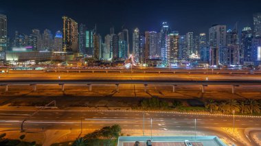 Dubai Marina gökdelenleri ve Şeyh Zayed yolu ile metro demiryolu hava akımının zaman çizelgesi. Otoparktaki arabalar. Modern kulelerin yakınındaki bir otoyolda trafik var, Birleşik Arap Emirlikleri