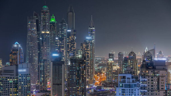 View of various illuminated skyscrapers in tallest recidential block in Dubai Marina aerial night timelapse with artificial canal. Many towers and yachts in harbor