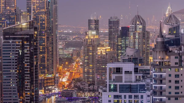Dubai Marina ve Medya Şehri 'nin modern gökdelenleri ve ofis binaları ile hava gününden geceye geçiş zamanı. Yeşil park yakınlarındaki üst geçitte trafik ve kavşak.