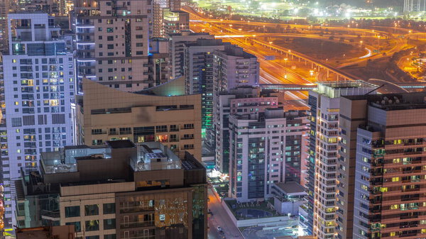 Dubai Marina luxury district with skyscrapers and towers near canal aerial night timelapse. Recidential buildings with construction site and traffic on streets