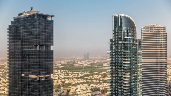 Tall residential buildings at JLT district aerial timelapse, part of the Dubai multi commodities centre mixed-use district. Villa houses and golf course on a background