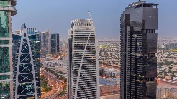 Tall residential buildings at JLT district aerial day to night transition timelapse, part of the Dubai multi commodities centre mixed-use district. Villa houses and road traffic on a background