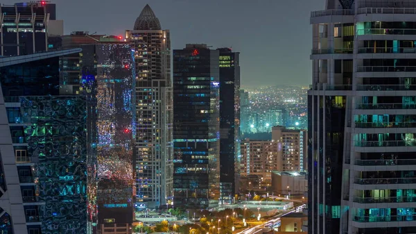 Tall residential buildings at JLT district aerial night timelapse, part of the Dubai multi commodities centre mixed-use district. Traffic between skyscrapers