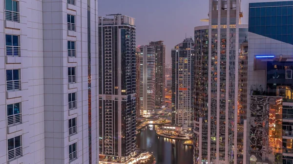 Tall residential buildings at JLT district aerial day to night transition timelapse, part of the Dubai multi commodities centre mixed-use district. Illuminated towers with glowing windows