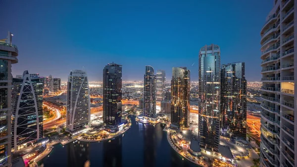 Tall residential buildings at JLT district aerial day to night transition timelapse, part of the Dubai multi commodities centre mixed-use district. Panoramic view to towers and skyscrapers