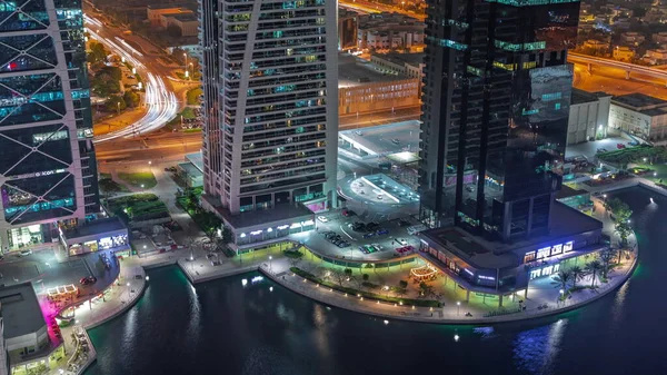 Tall residential buildings at JLT district aerial night timelapse, part of the Dubai multi commodities centre mixed-use district. Parking on intersection and car parking