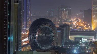 Geleceğin Müzesi uzay sergisi ikonik torus şekilli gece hava zaman çizelgesi. Paslanmaz çelik cephesi ve Arapça bir şiir oluşturan pencereler.