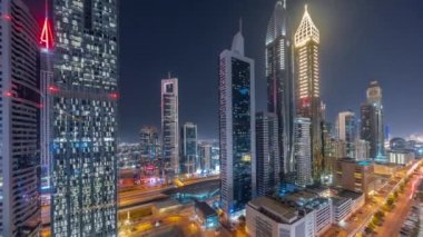 Dubai Uluslararası Finans Bölgesi 'nin panoramik hava manzarası ve birçok gökdelen gece zaman çizelgesi. Çok katlı otoparkların yakınında, aydınlık kuleleri olan bir yolda trafik vardı. Dubai, BAE.