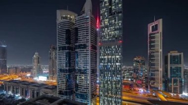 Panorama, Dubai Uluslararası Finans Bölgesi 'nin gökdelenler tarafından aydınlatılmış gece zaman çizelgesini gösteriyor. Çok katlı otoparkların yakınındaki bir yolda trafik vardı. Dubai, BAE.