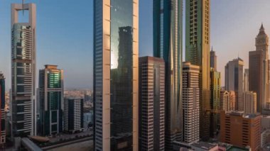 Gündoğumunda gökdelenlerden yansıyan güneşli Dubai Uluslararası Finans Bölgesi 'nin hava görüntüsü. Çatıda yüzme havuzu olan çok katlı otoparkın yakınındaki bir yolda trafik vardı. Dubai, BAE.