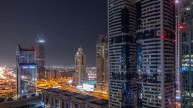 Dubai Uluslararası Finans Bölgesi 'nin tüm gece boyunca birçok gökdeleni olan hava manzarası. Işıkları sönmüş kulelerle çevrili bir otoyol kavşağında trafik vardı. Dubai